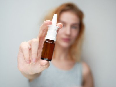 Eine Frau hält ein Nasenspray mit ausgestrecktem Arm vor sich