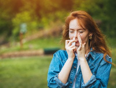 Eine Frau wendet Nasenspray im rechten Nasenloch an