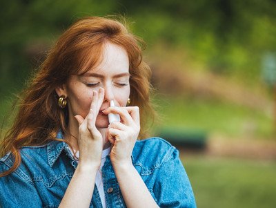 Eine Frau wendet Nasenspray im linken Nasenloch an