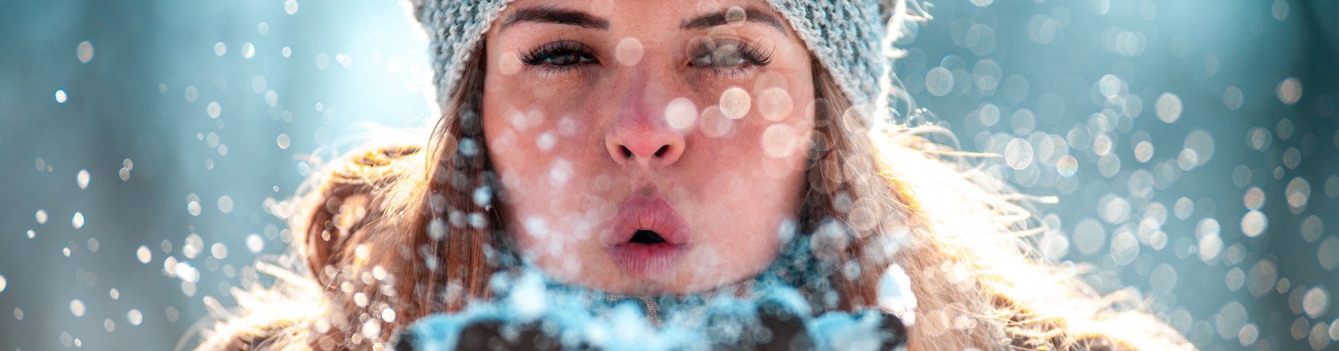 [Translate to Deutsch (Österreich):] Frau mit Mütze pustet Schnee in die Kamera
